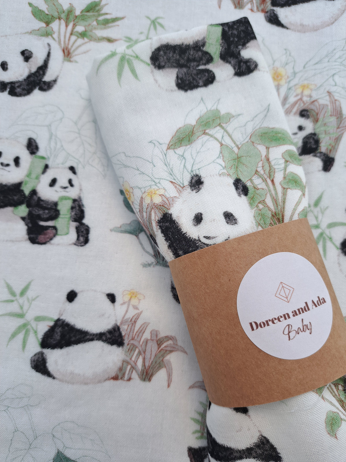 Close-up of panda and bamboo muslin square rolled with Doreen and Ada Baby band showing watercolour giant panda and wildflower detail