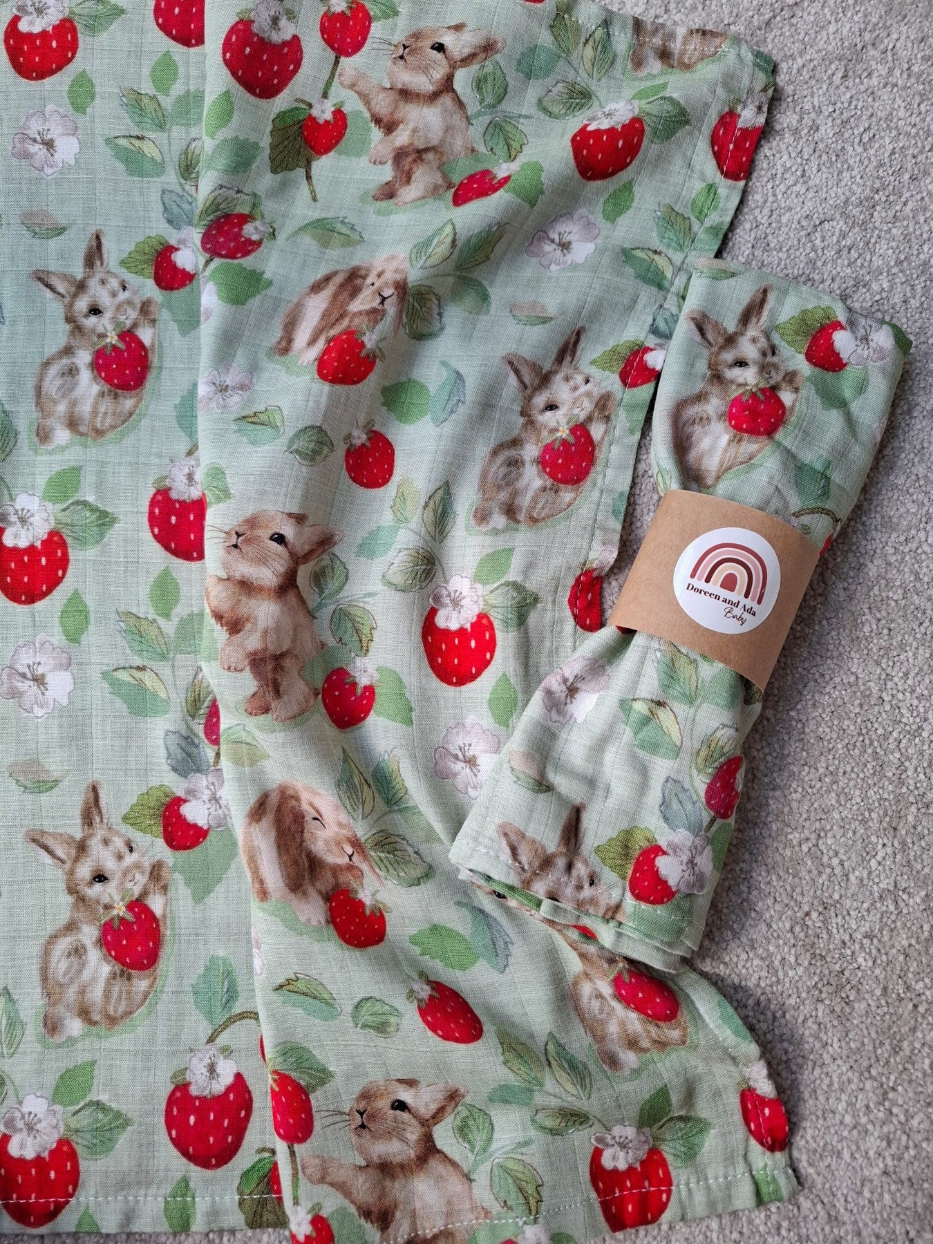 Flat lay of muslin square featuring a whimsical pattern of bunnies and strawberries on mint green soft cotton fabric