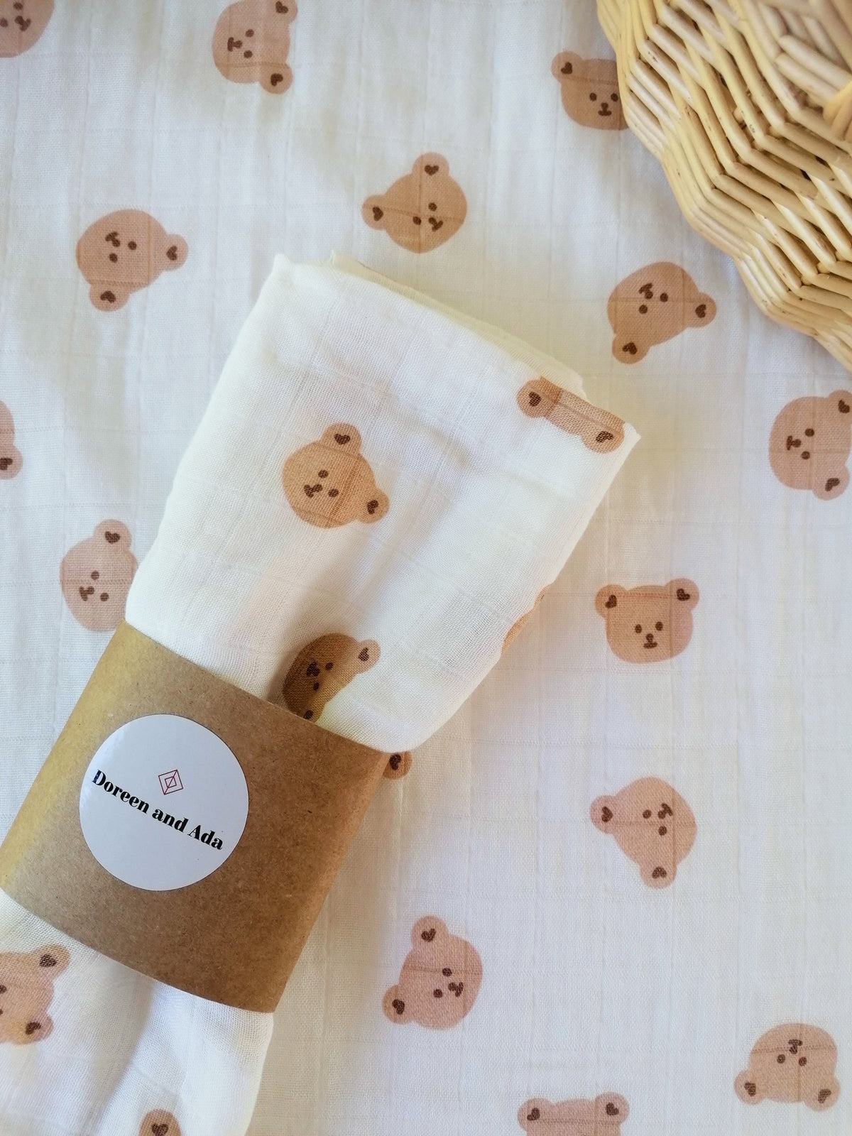 Teddy bears picnic muslin swaddle rolled with Doreen and Ada kraft paper band on matching teddy bear print background with wicker basket