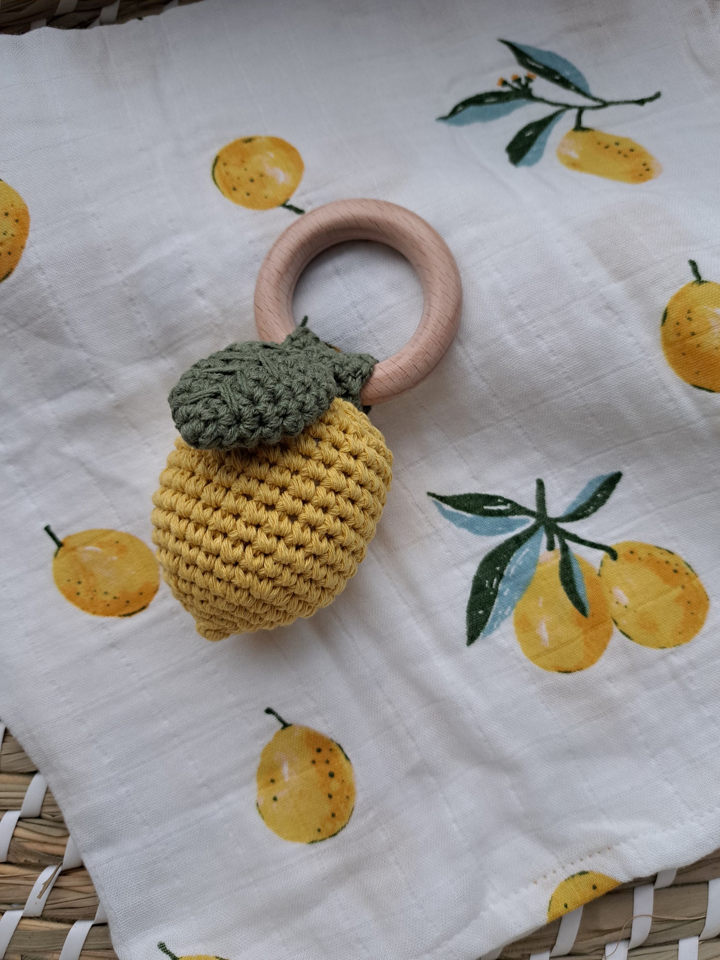 A yellow lemon-shaped rattle with a green stem, made from wood and cotton, displayed on a white background with yellow lemon prints.