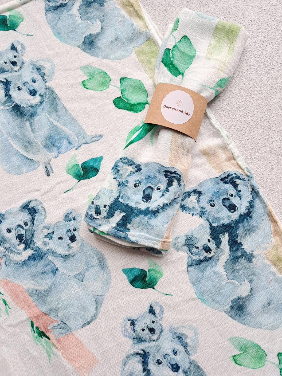 Koala and eucalyptus muslin square rolled with Doreen and Ada kraft paper band on unfolded koala print muslin showing scale of 60cm square