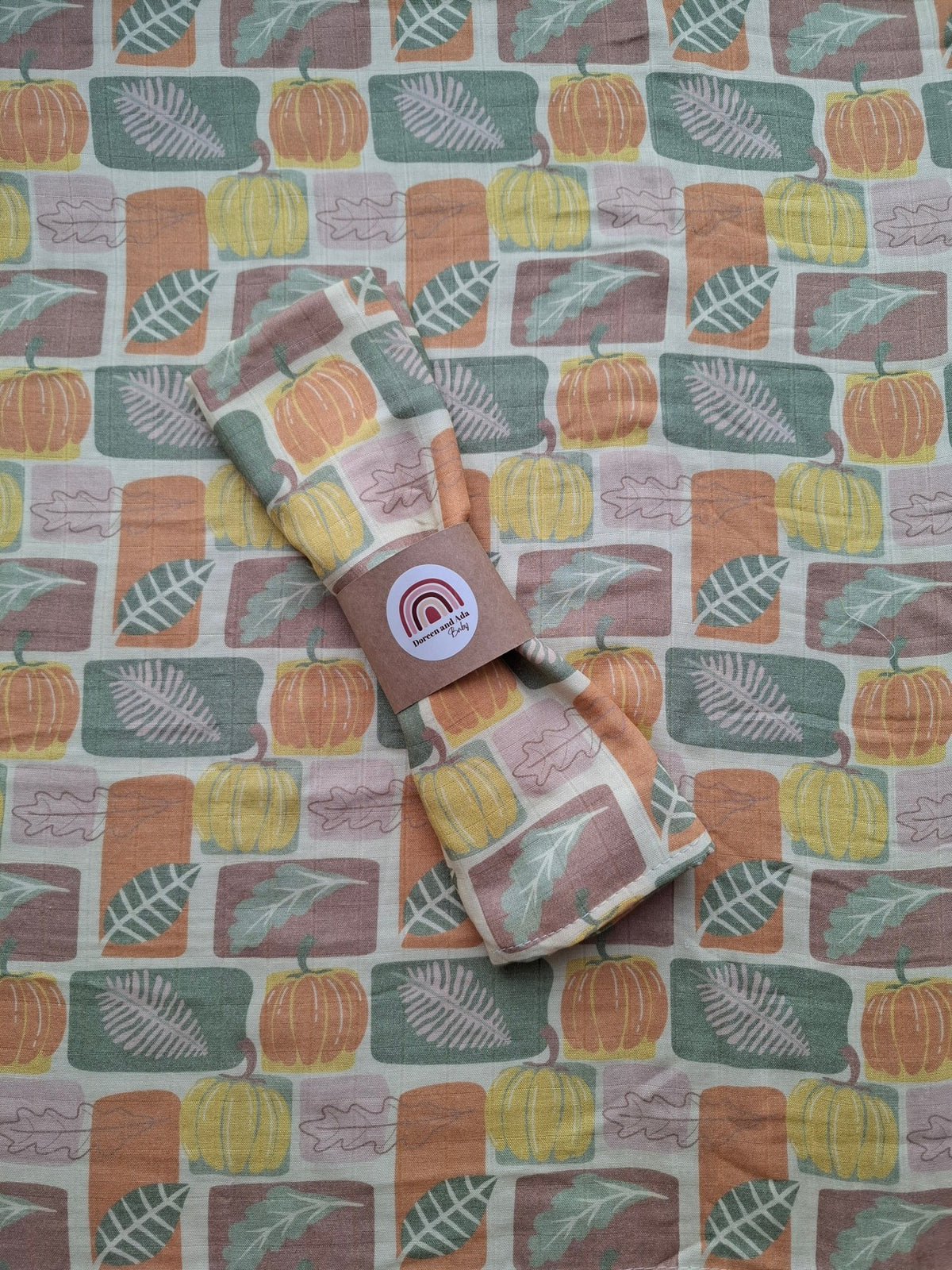 Muslin square featuring a pattern of pumpkins and leaves in earthy autumn colours