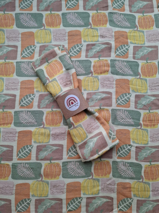 Muslin square featuring a pattern of pumpkins and leaves in earthy autumn colours