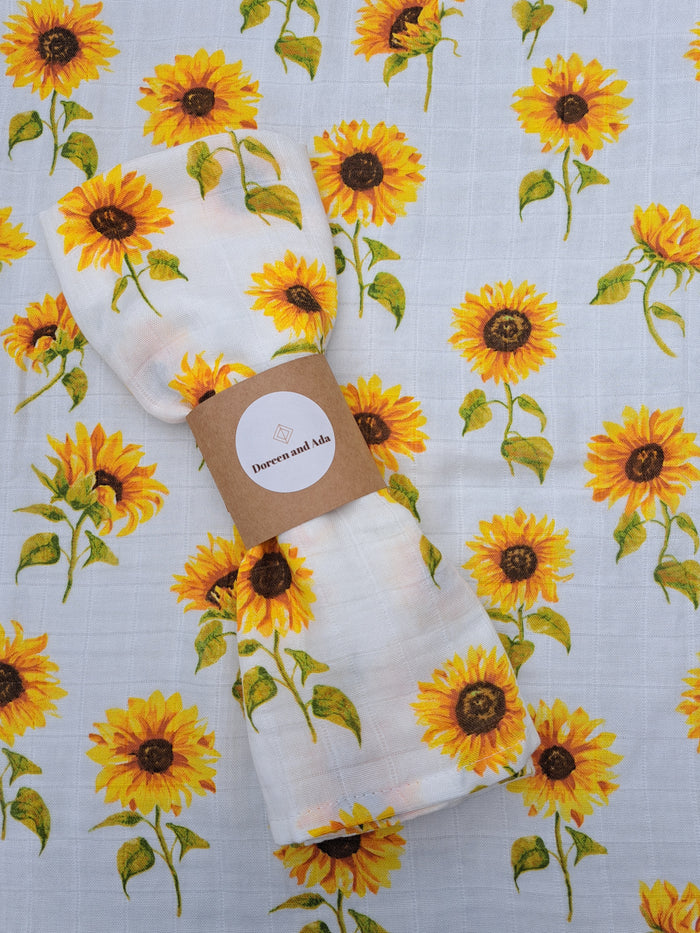 A folded white muslin square with a sunflower pattern, placed on a table with a similar patterned background.