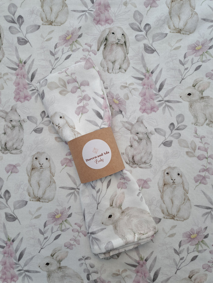 A white cotton muslin square with a floral and rabbit pattern, displayed on a flat surface.