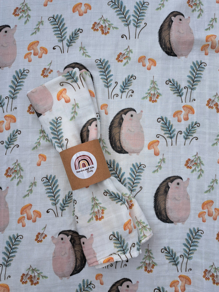 A small muslin square with a hedgehog pattern, predominantly in shades of white, beige, and green, with a floral border.