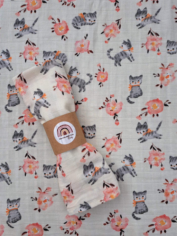 A beige muslin square with a pink cherry blossom and cat pattern, displayed with a brand tag showing a cat and cherry blossom design.