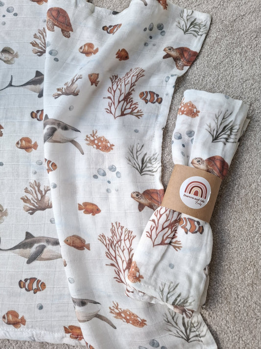 Rolled Ocean Friends muslin square showing turtles and coral design on soft white cotton background