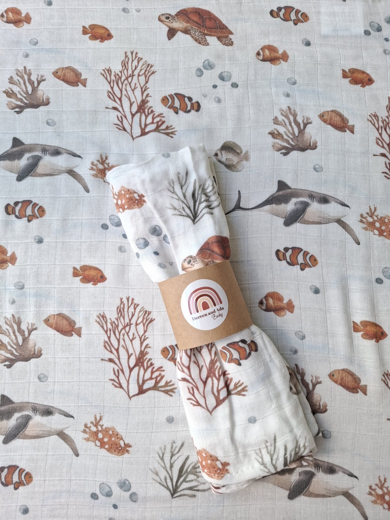 Flat lay of Ocean Friends muslin cloth partially opened alongside rolled muslin on grey carpet