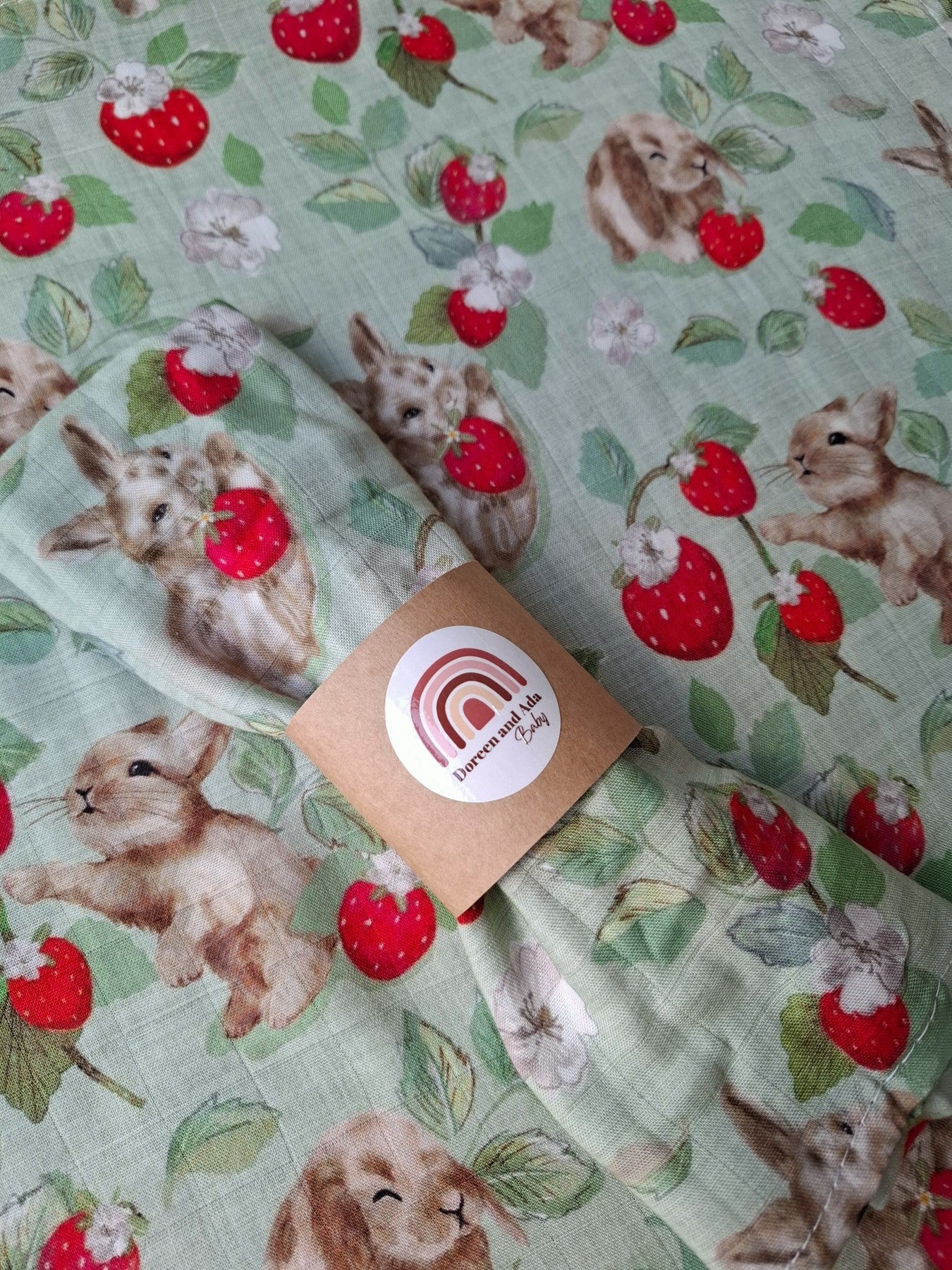 Close-up of folded muslin square showing playful bunnies and bright red strawberries on soft mint cotton