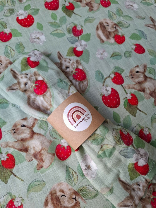 Close-up of folded muslin square showing playful bunnies and bright red strawberries on soft mint cotton