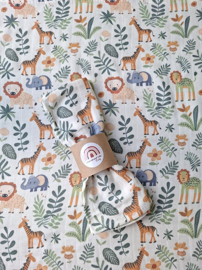 Muslin square featuring a printed pattern of giraffes, lions and elephants with green leaves and orange flowers on soft cotton fabric