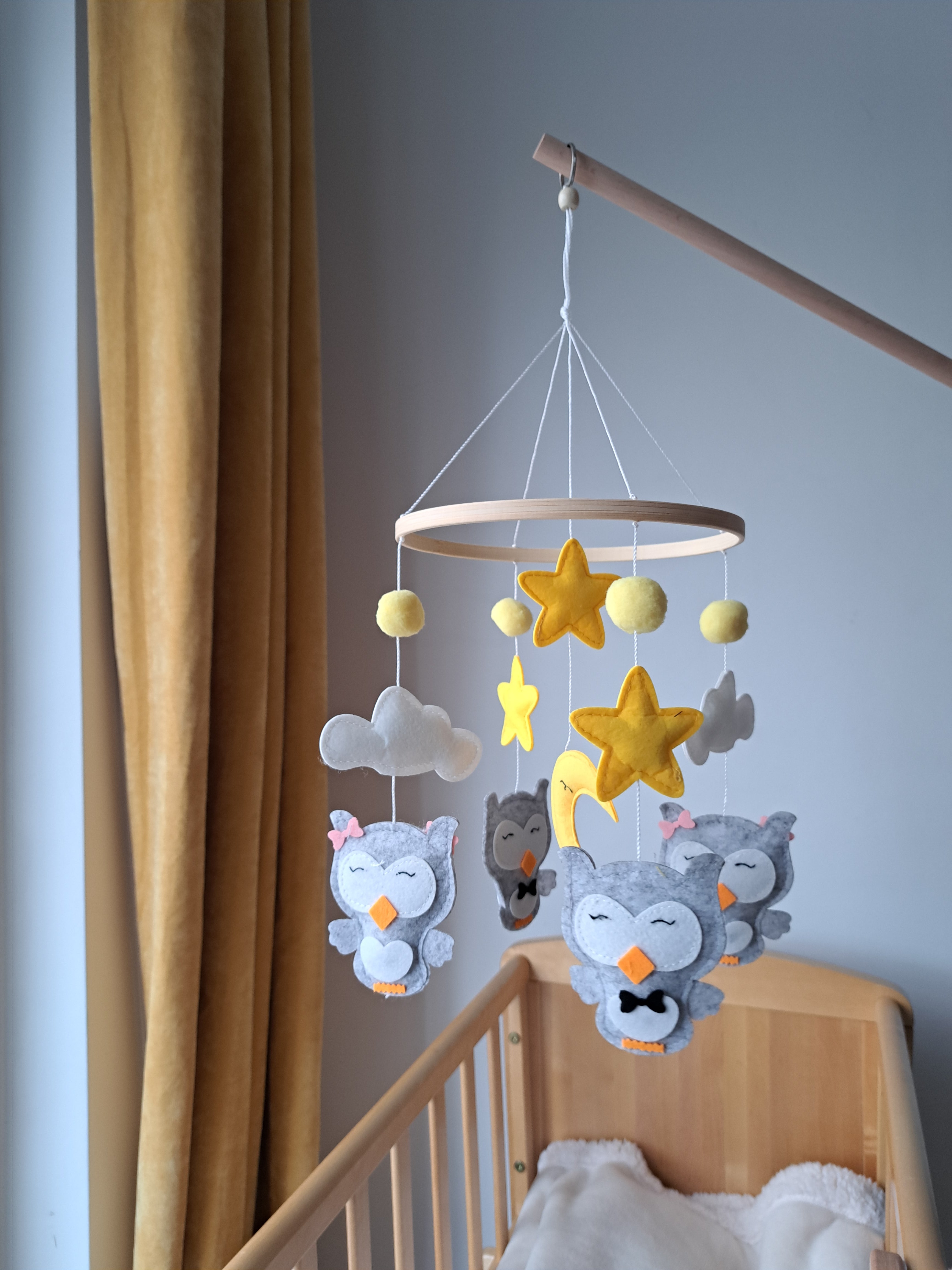 A decorative baby mobile featuring owl and bird figures, clouds, and stars hanging above a crib.