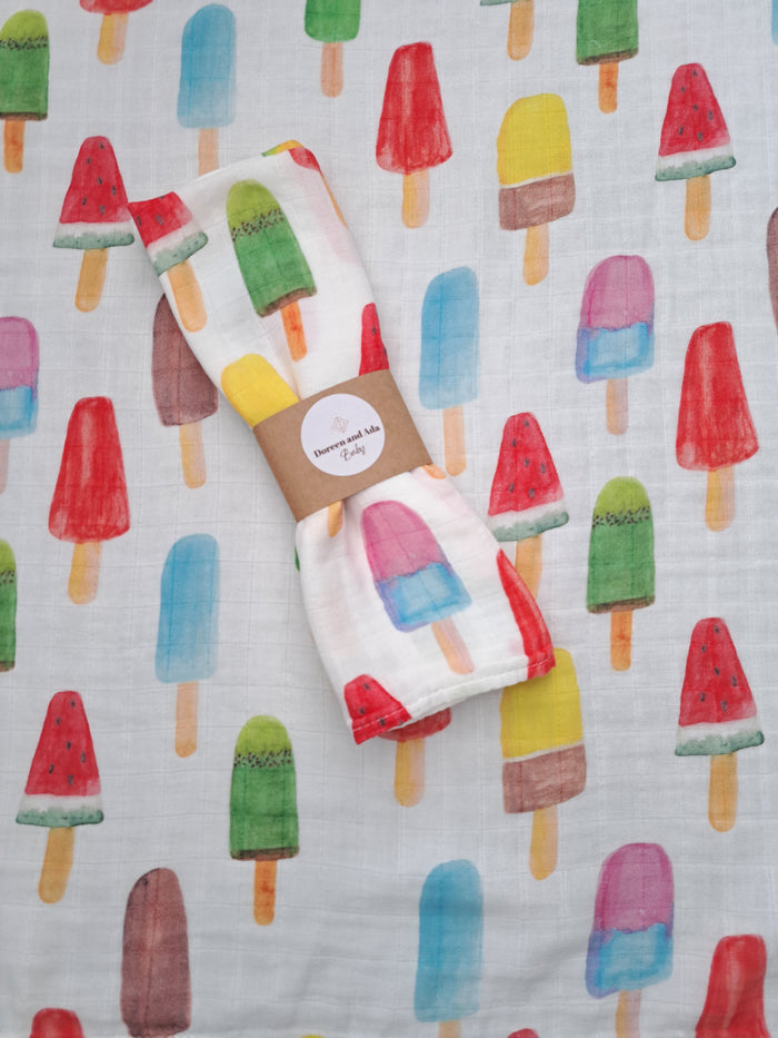 A cotton and bamboo muslin square with a colorful ice cream pattern, displayed on a similar patterned background.