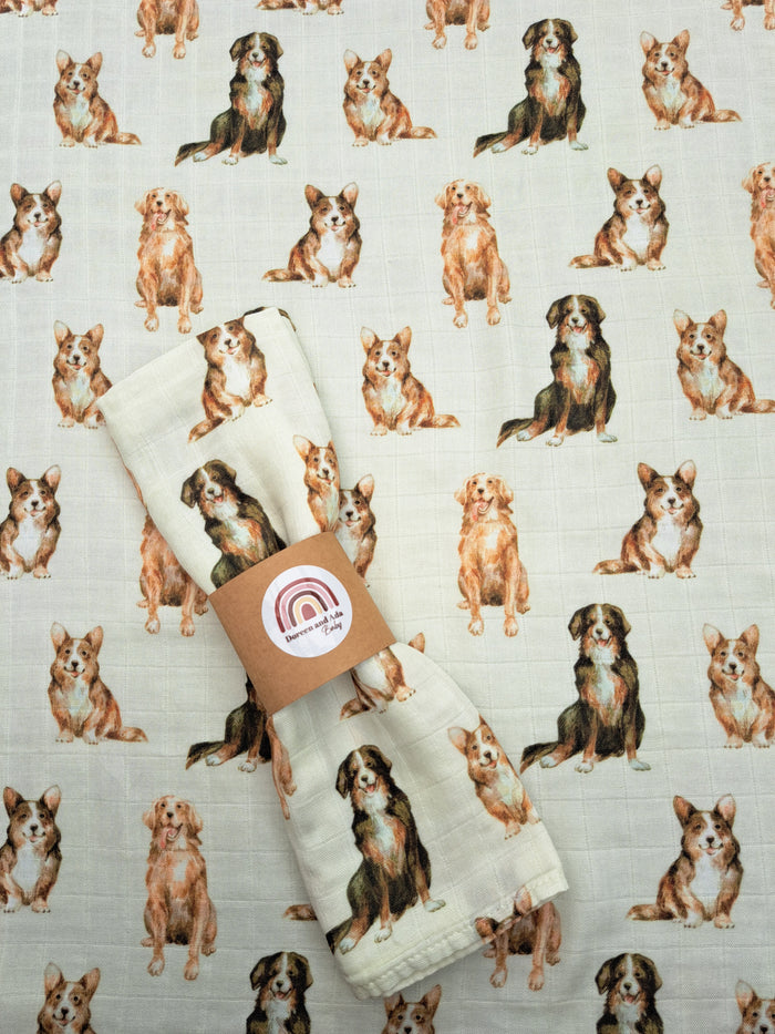 A beige muslin square with a pattern of cartoon dogs on it, likely used for baby swaddling or as a receiving blanket.