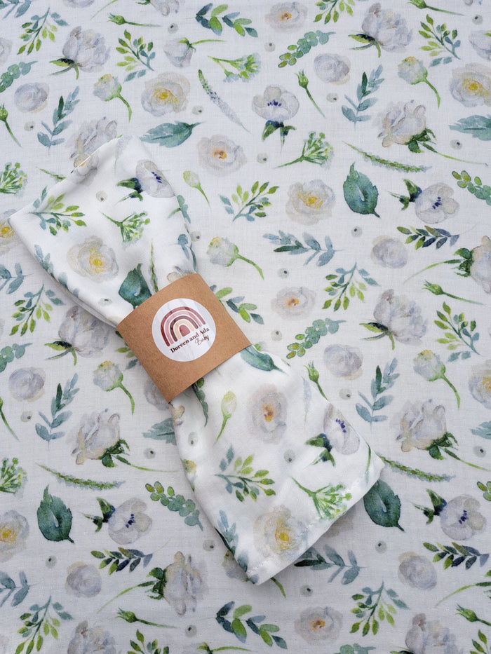 A white muslin square with a floral pattern, featuring a rose and peony design, laid flat on a similar patterned background.